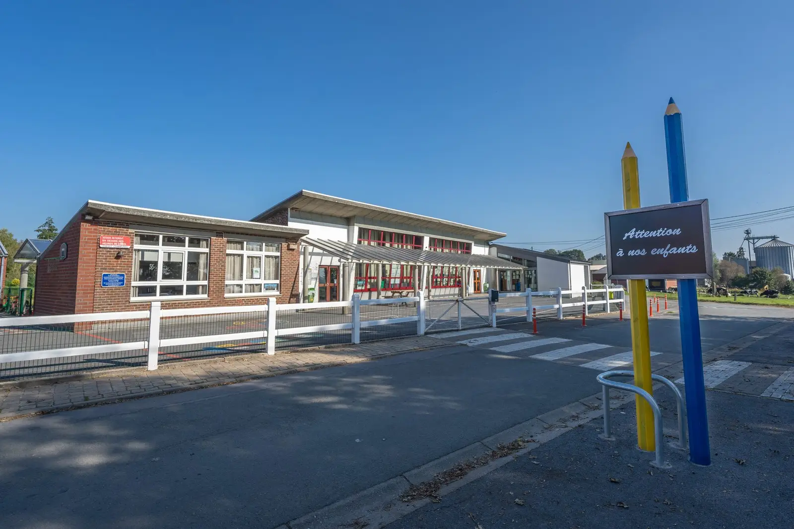 L'entrée de l'école, avec ses crayons géants et le panneau « Attention à nos enfants »